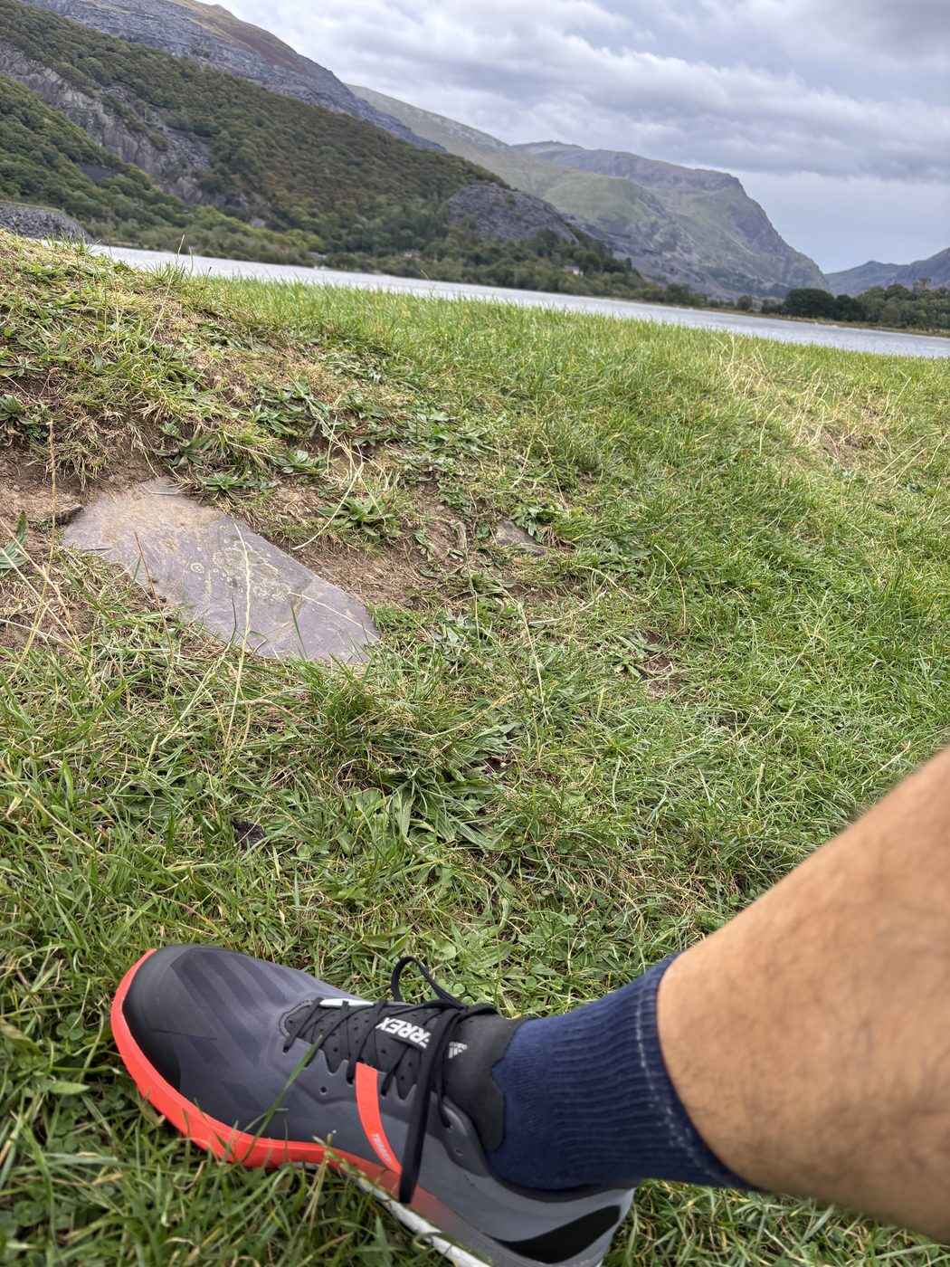 Pause beim Laufen nach der Schicht: Blick über einen See auf die Berge von Snowdonia, im Vordergrund ein Laufschuh im Gras